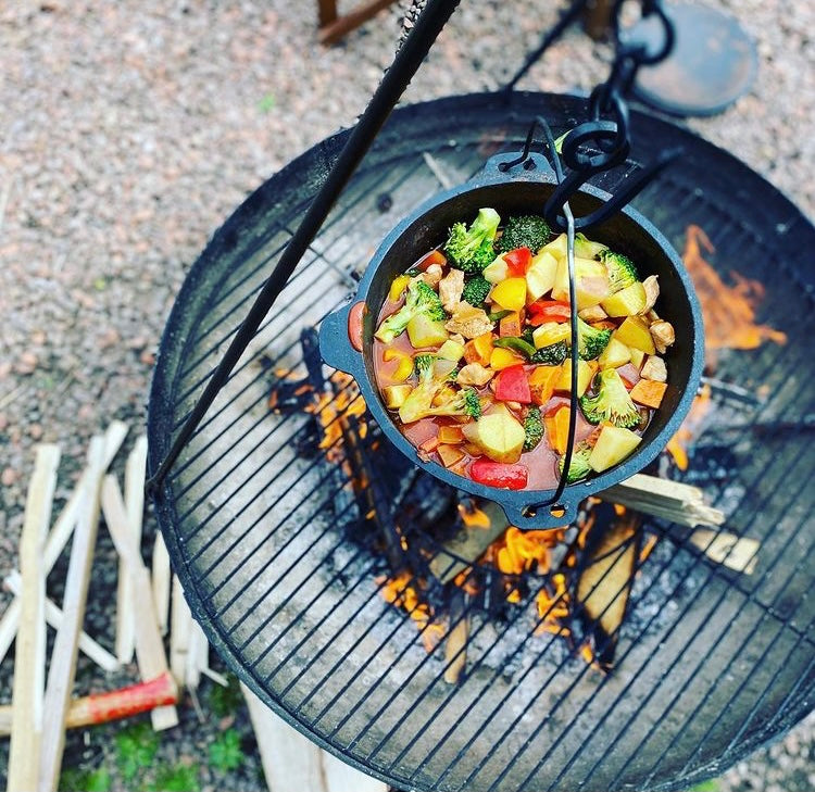Vegetables in a pot cooking over an outdoor firepit